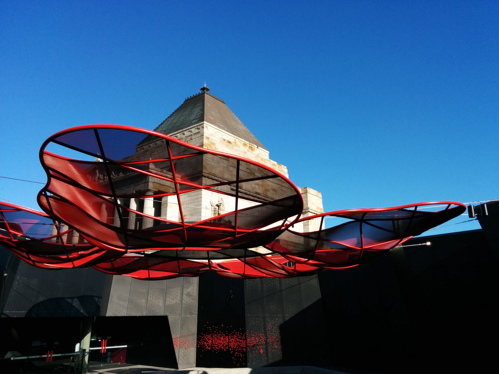 Large red steel and mesh poppy canopy suspended in front of the Shrine of Remembrance